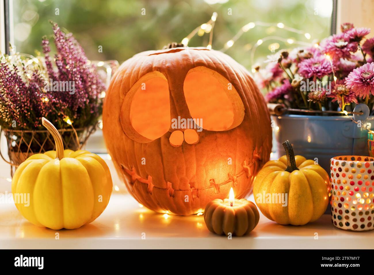 Halloween decoration of Jack O' Lantern with pumpkins and flowers near candle on window sill Stock Photo