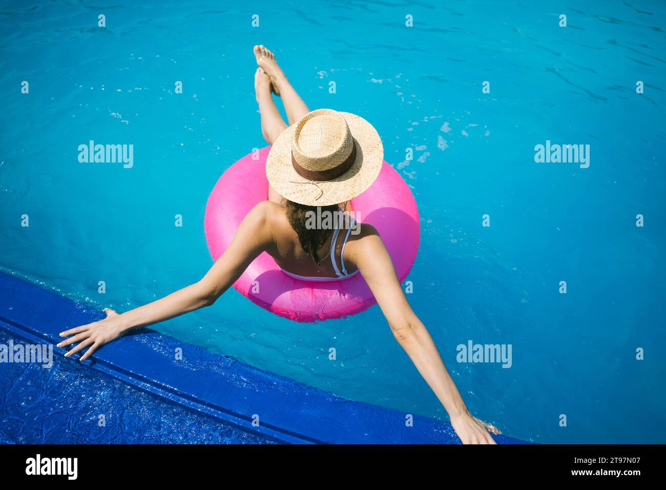 Woman wearing straw hat relaxing on inflatable swim ring in pool Stock Photo