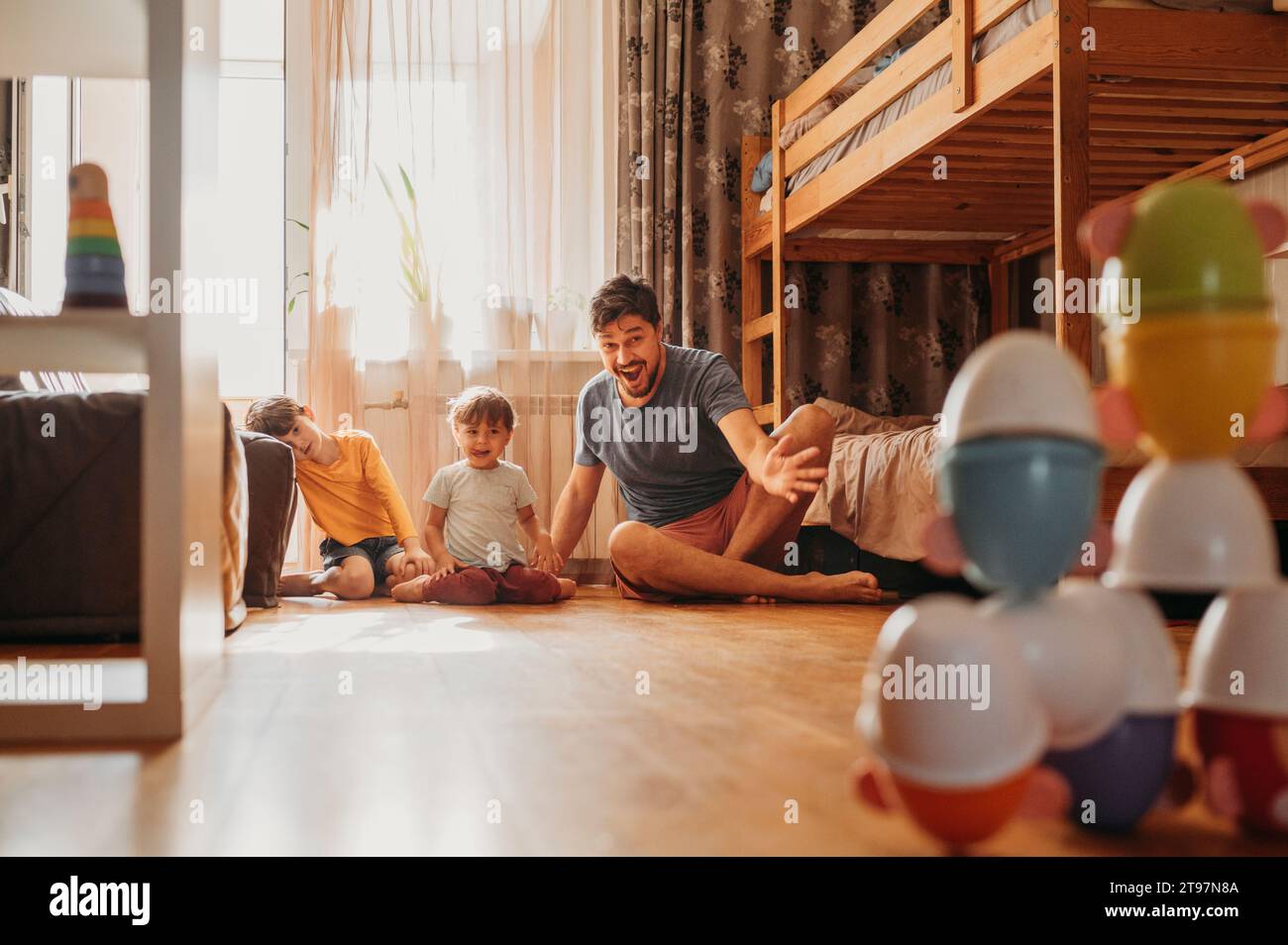 Cheerful father playing bowling game with sons at home Stock Photo