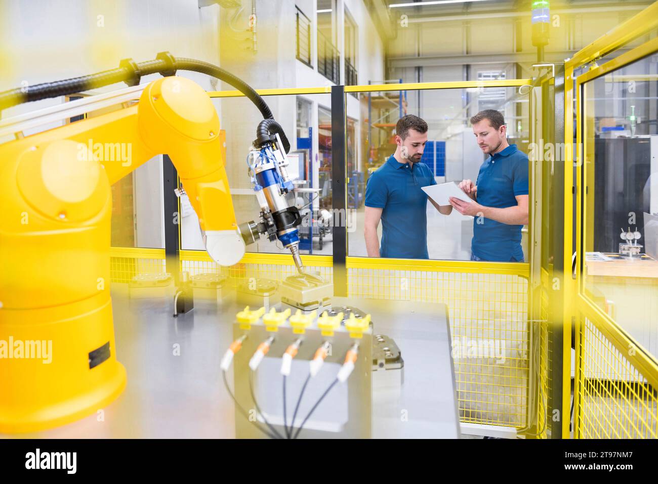 Robotic arm with engineer showing tablet PC to colleague at factory Stock Photo