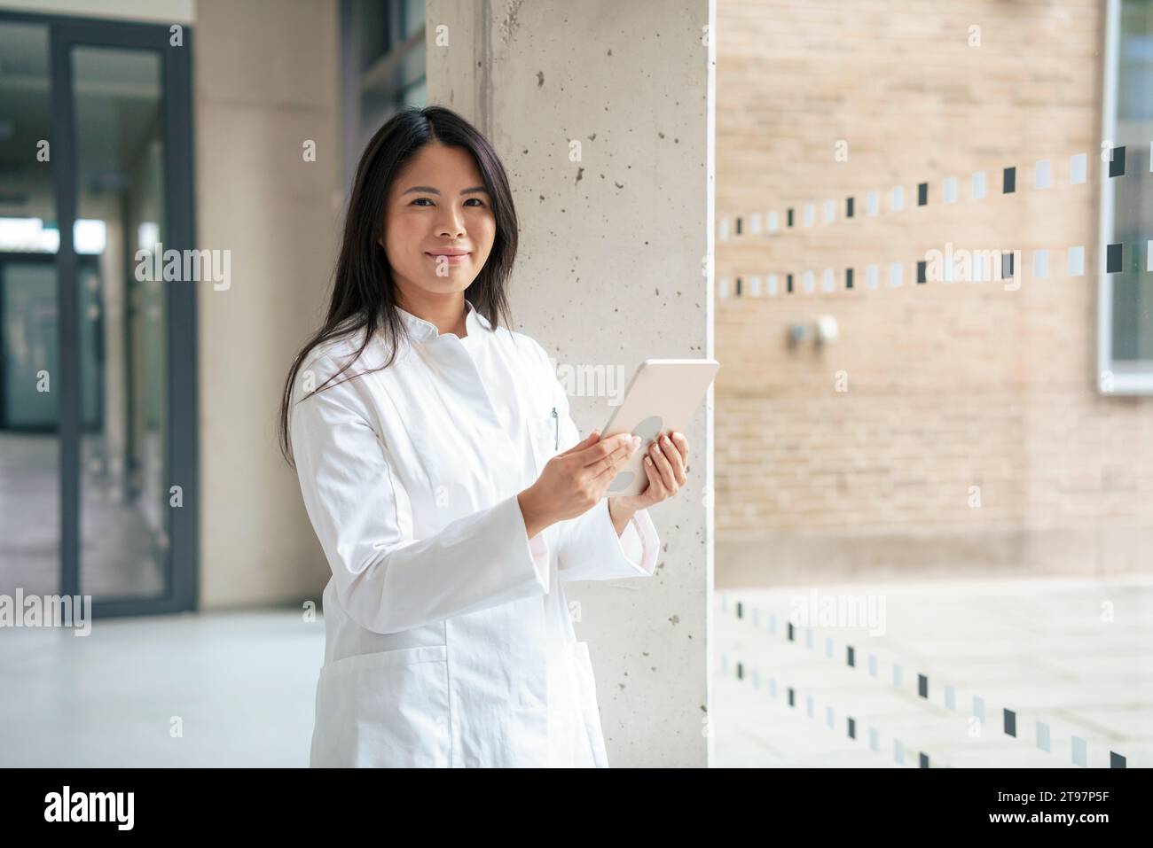Smiling scientist standing with tablet PC in corridor Stock Photo
