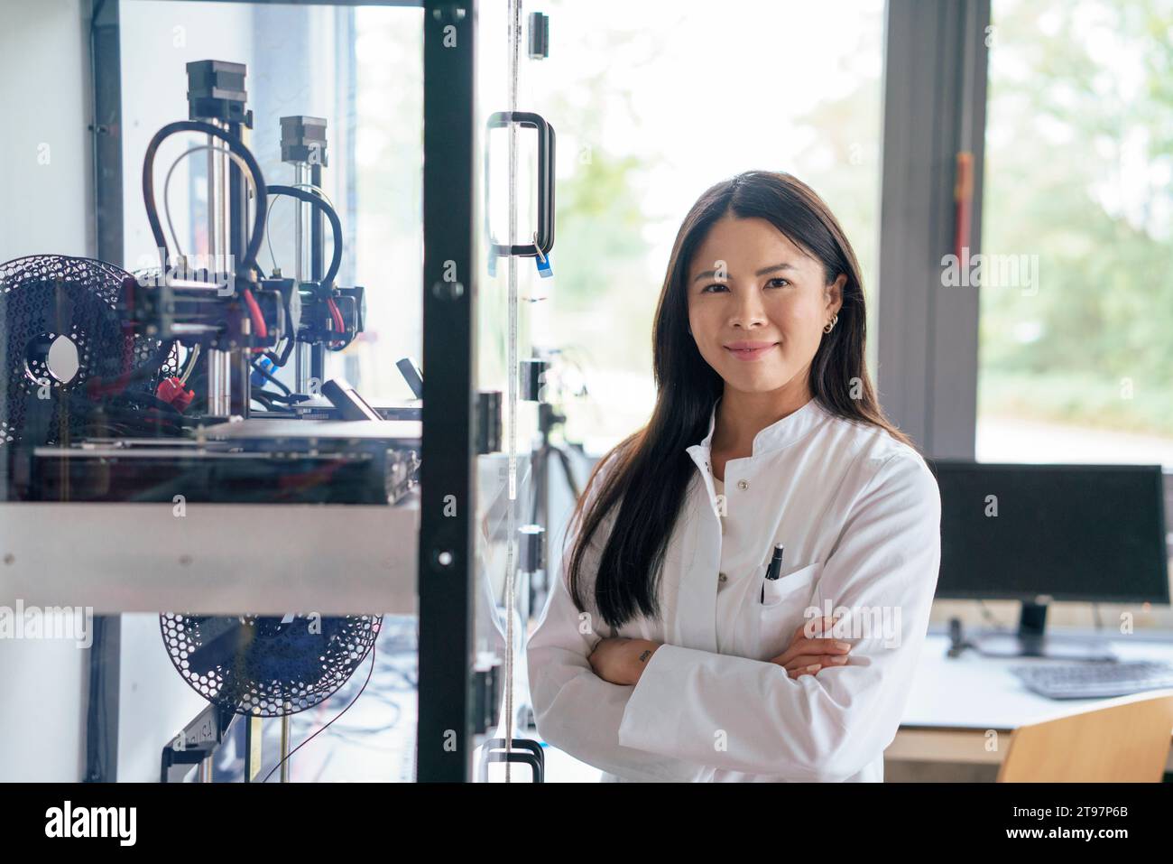 Smiling scientist standing with arms crossed near machine in laboratory Stock Photo