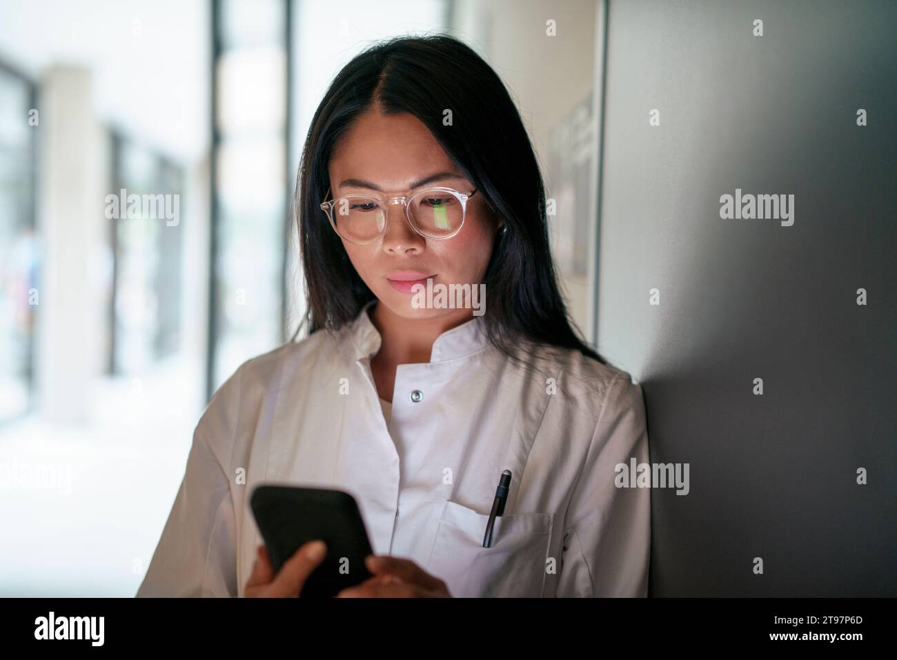 Scientist wearing eyeglasses and using smart phone in corridor Stock Photo
