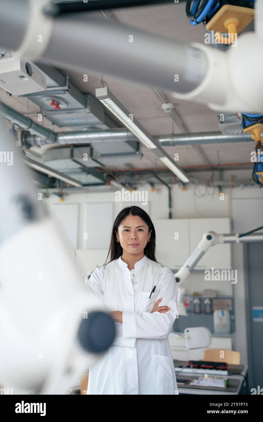 Scientist standing with arms crossed in laboratory near robotic arms Stock Photo
