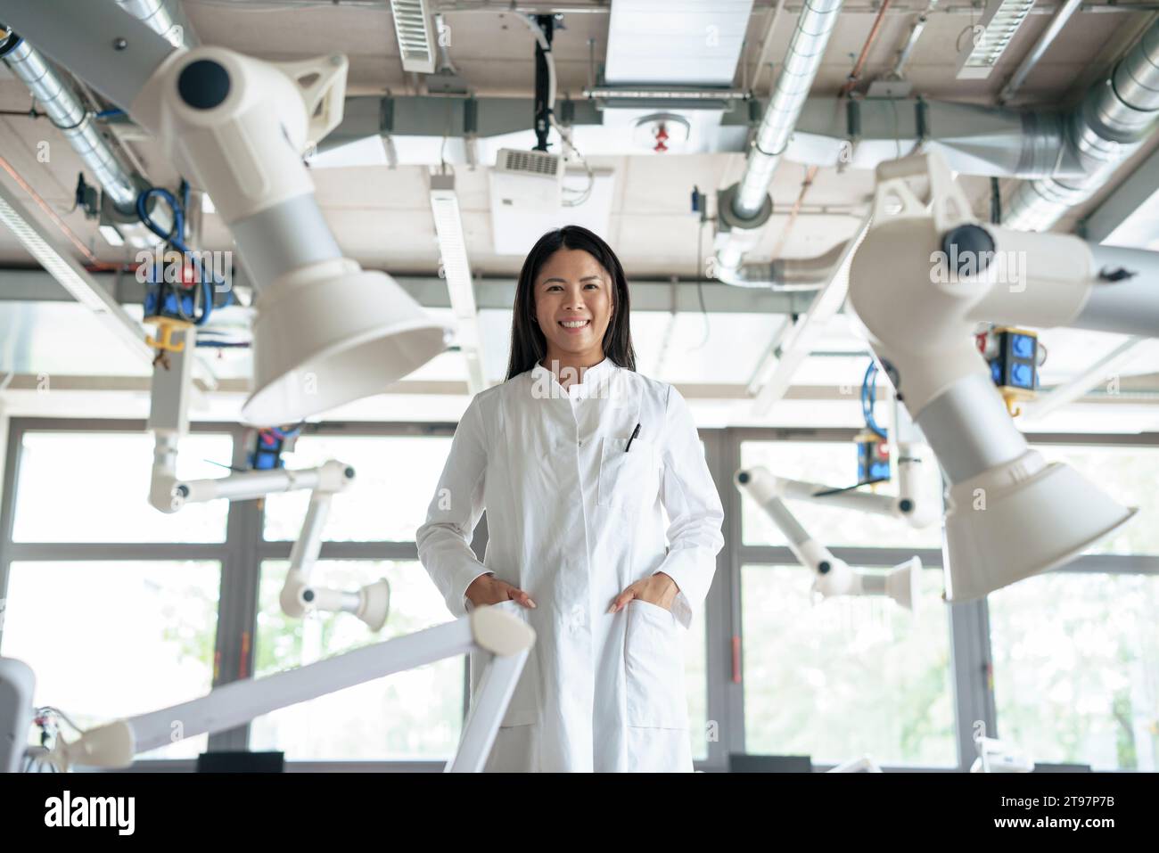 Happy scientist standing amidst robotic arms Stock Photo