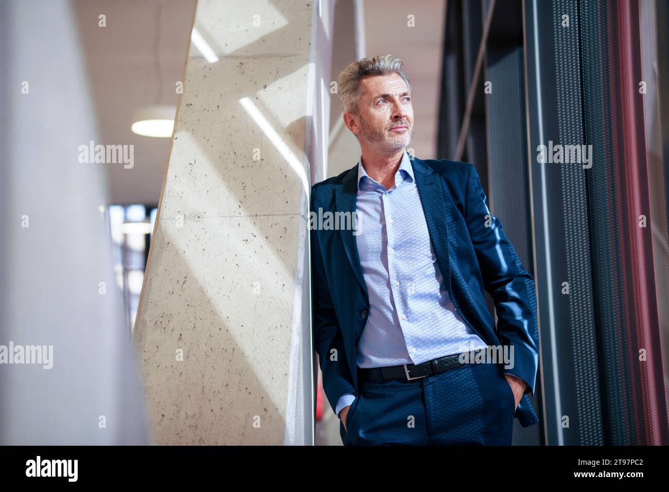 Thoughtful businessman with hands in pockets standing near column Stock Photo
