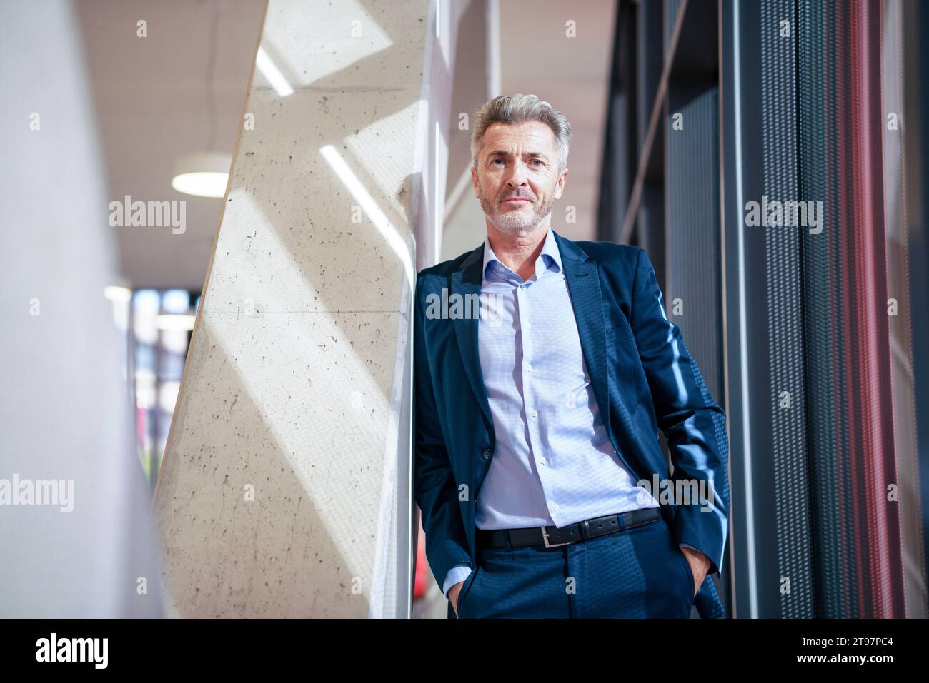 Mature businessman with hands in pockets standing near column Stock Photo