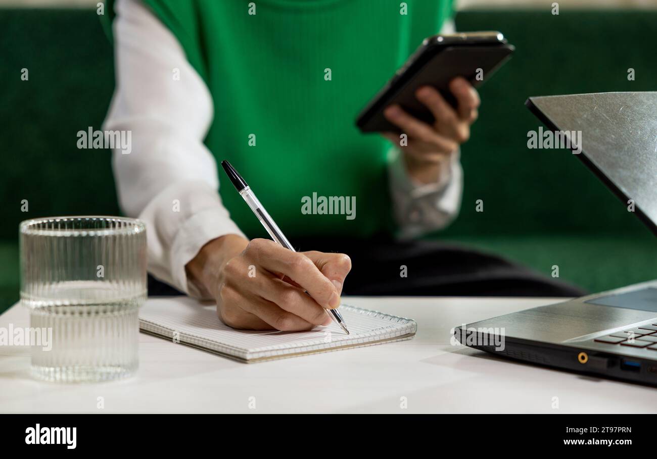 Freelancer taking notes from smart phone at home office Stock Photo