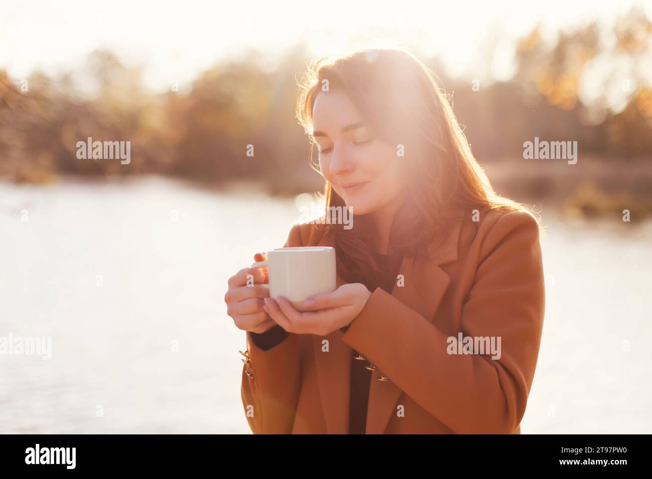Happy woman holding cup of tea near lake Stock Photo