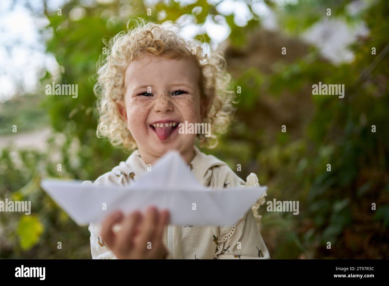 Happy girl sticking out tongue and holding paper boat Stock Photo