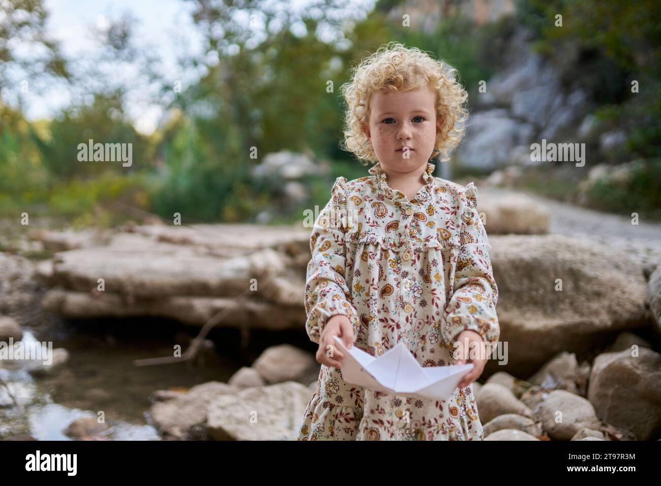 Cute girl holding paper boat standing near rocks Stock Photo