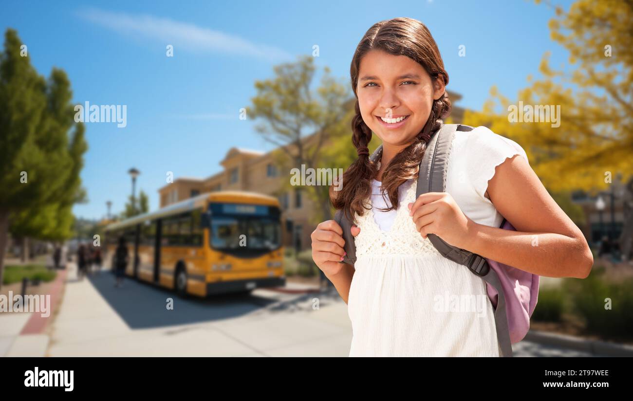 Happy Young Hispanic Girl Wearing a Backpack Near a School Bus on