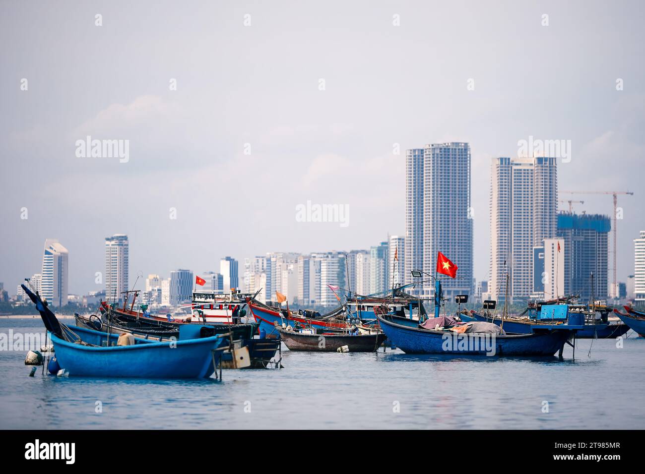 Selective focus on Vietnamese flag on fishing boat moored in port against coast with modern buildings. Da Nang cityscape in Vietnam. Stock Photo