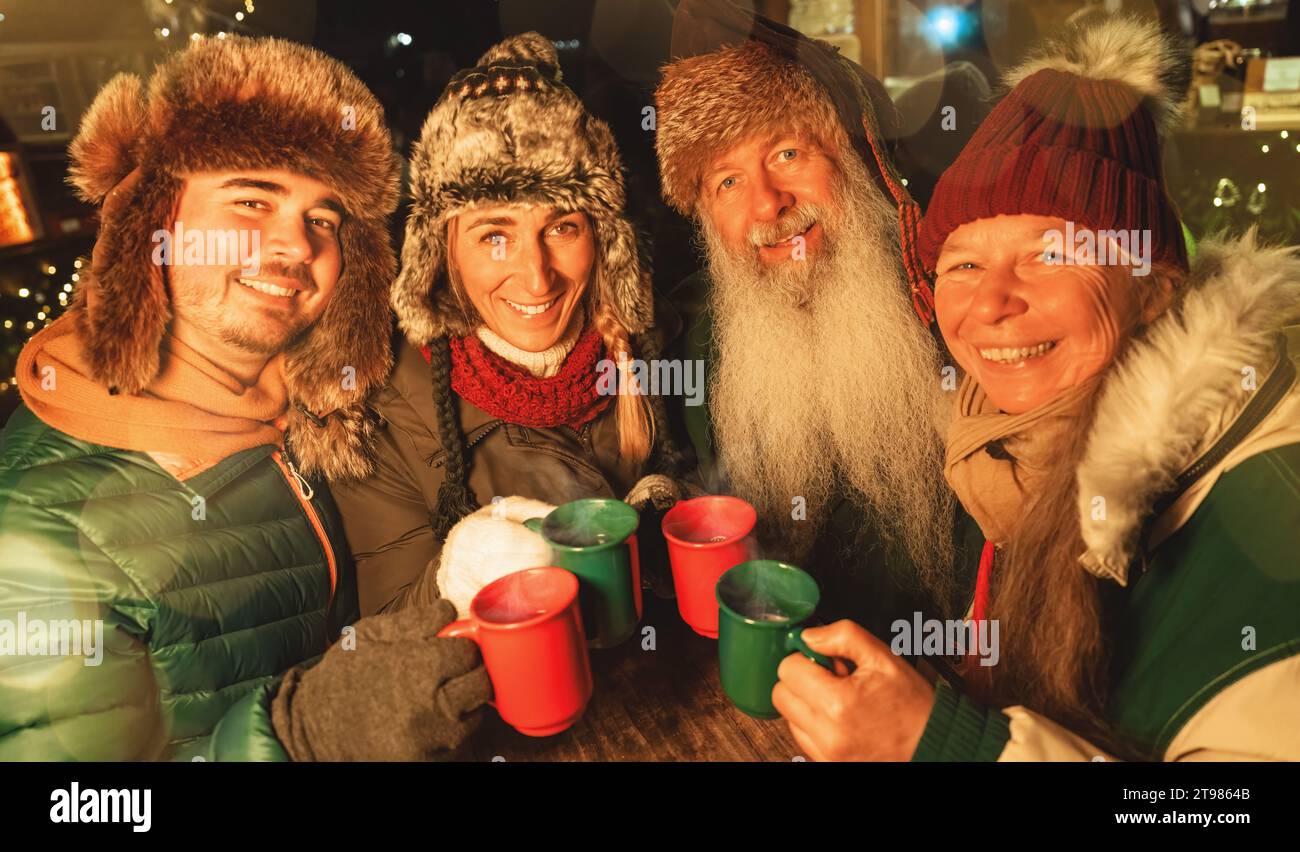 Happy family toasting with mugs of mulled wine and hot chocolate at a Christmas market, wearing winter hats Stock Photo