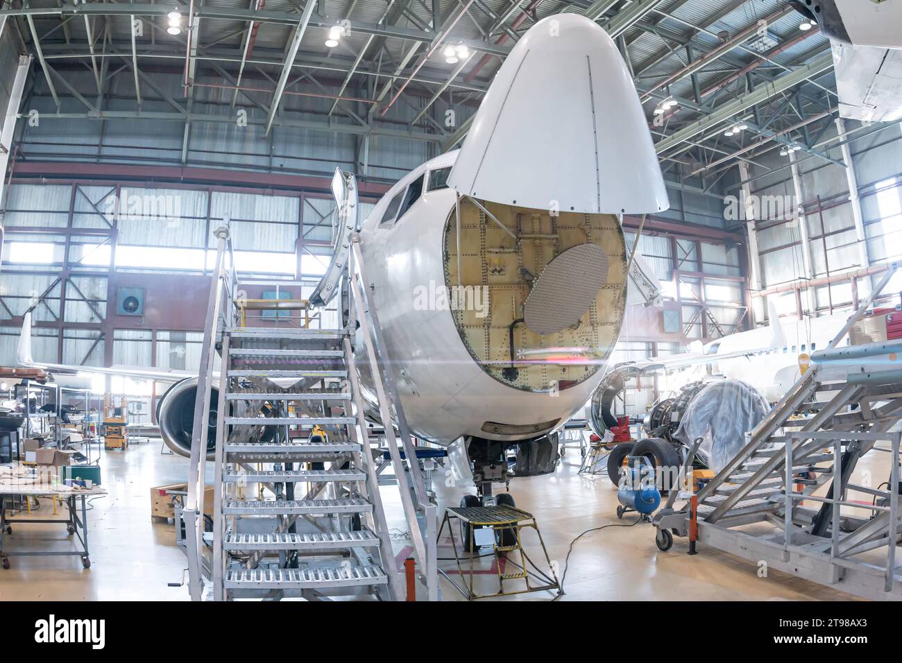 Front view of the white passenger airplane under maintenance in the aviation hangar. The aircraft has opened weather radar. Checking mechanical system Stock Photo