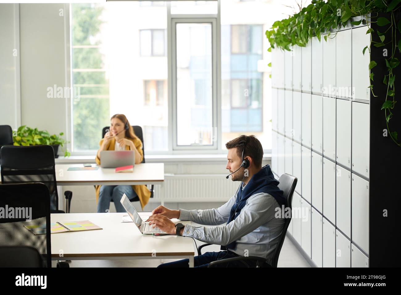 Young managers with laptops at their workplaces communicate using headset Stock Photo