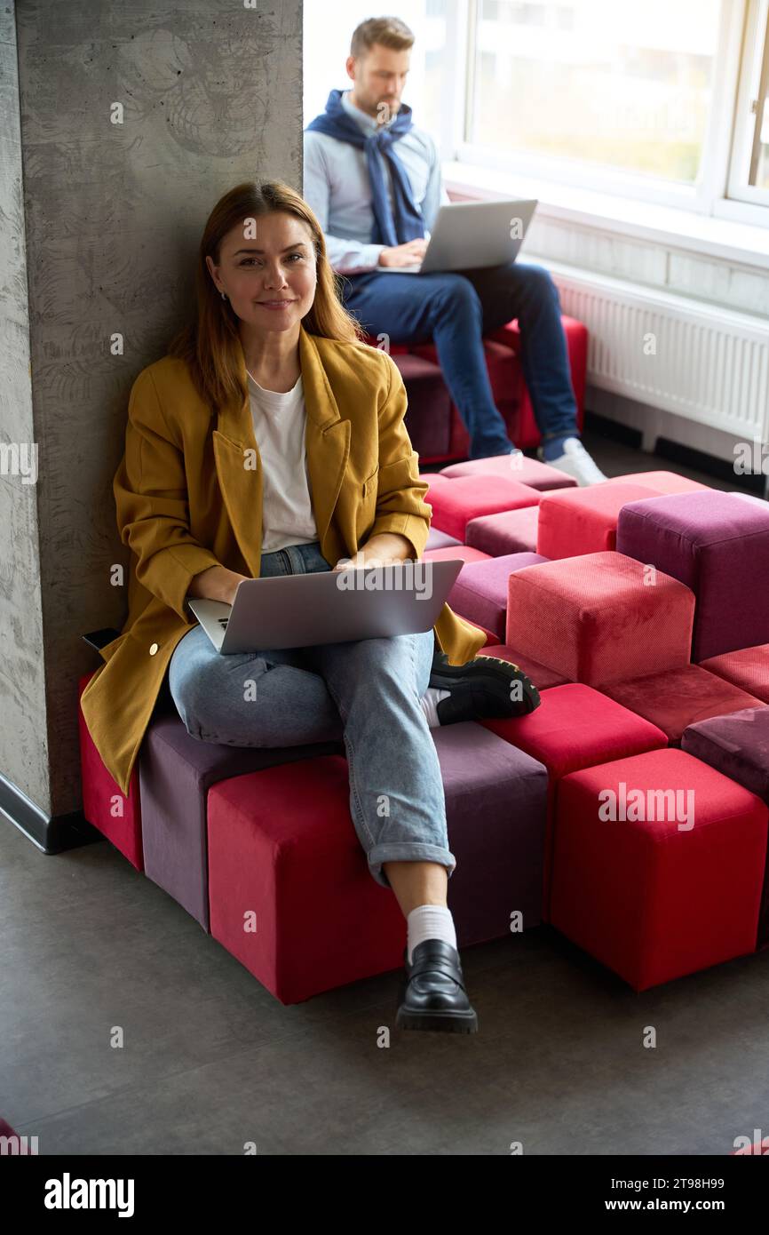 Colleagues sit with laptops on colorful sofas Stock Photo