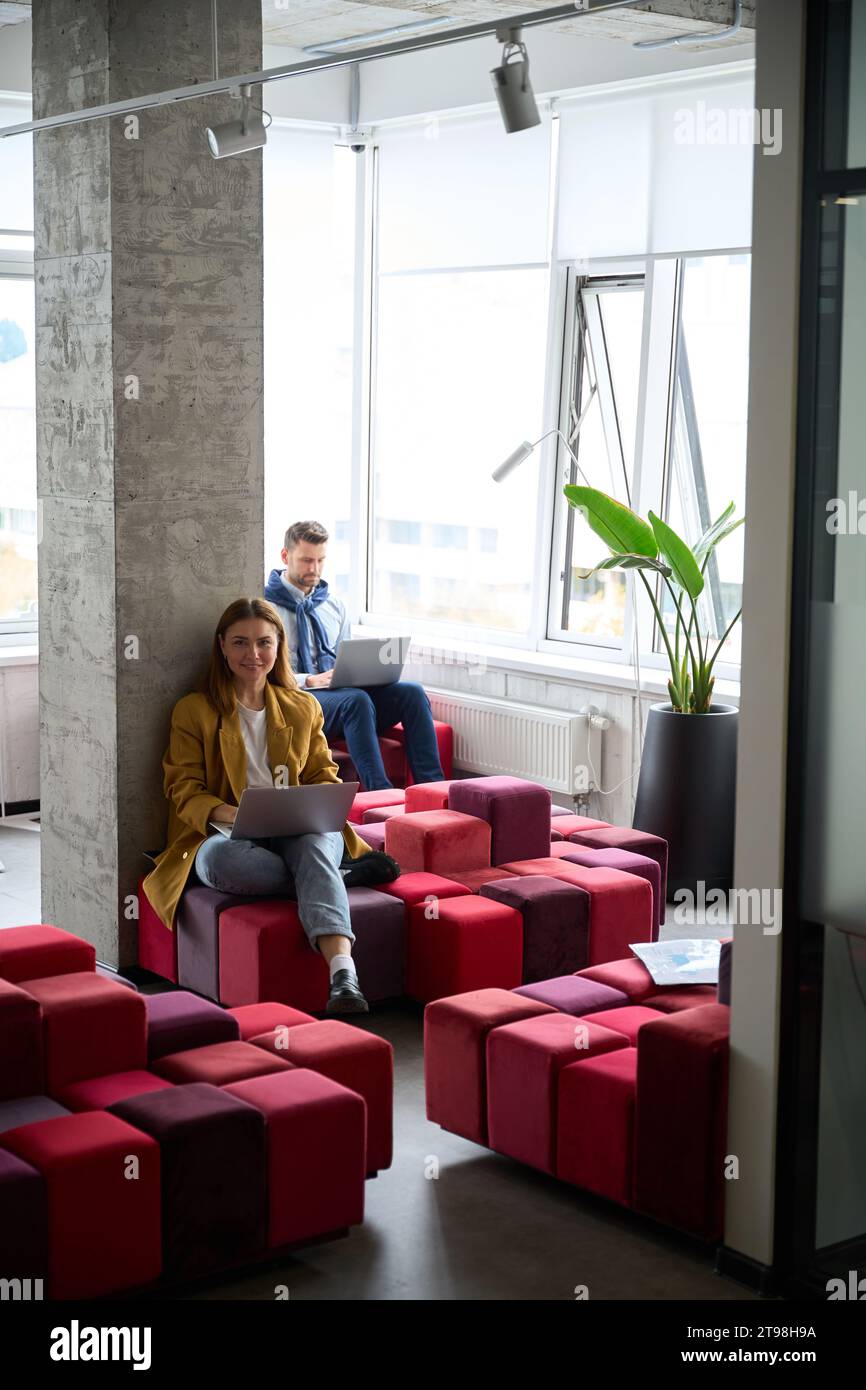 Colleagues managers sit with laptops on multi-colored sofas Stock Photo