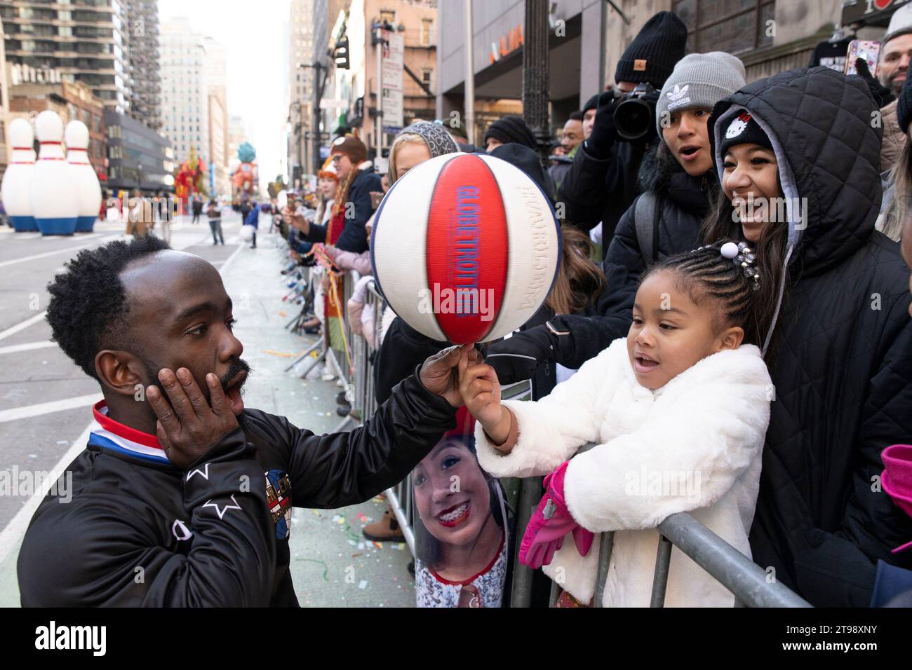 Brenda Bauchman, 4 watches as Hot Shot Swanson from the Harlem Globetrotters places a spinning basketball on her thumb as her family watches, during the Macys Thanksgiving Day Parade on Thursday November 23, in Manhattan, New York. (Photo by Mattie Neretin/Sipa USA). Credit: Sipa USA/Alamy Live News Stock Photo