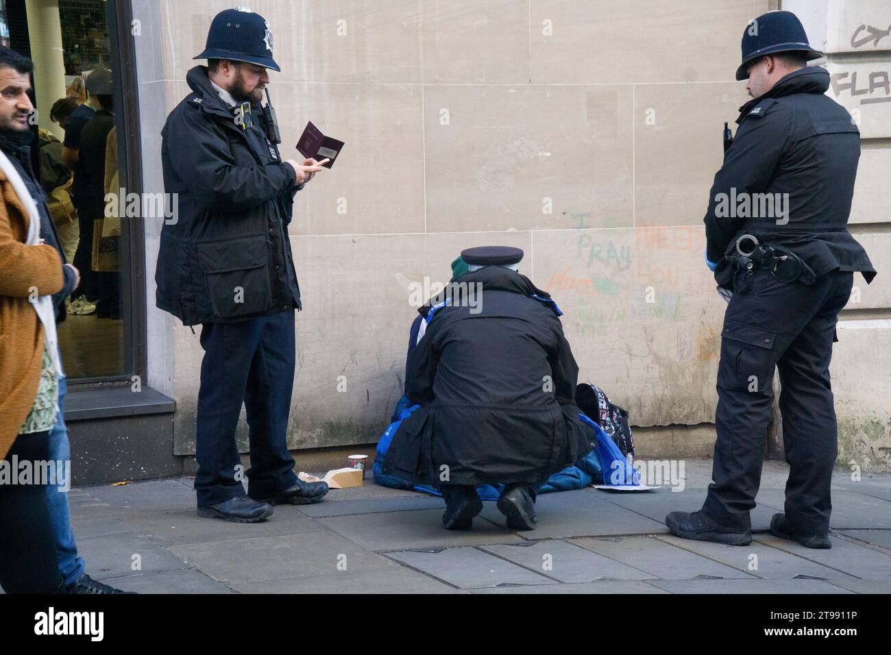 London, UK. 23rd Nov, 2023. Three police officers check the passport of a person who was begging on Long Acre, Covent Garden, having torn up the sign he was holding which said they were hungry. Credit: Anna Watson/Alamy Live News Stock Photo