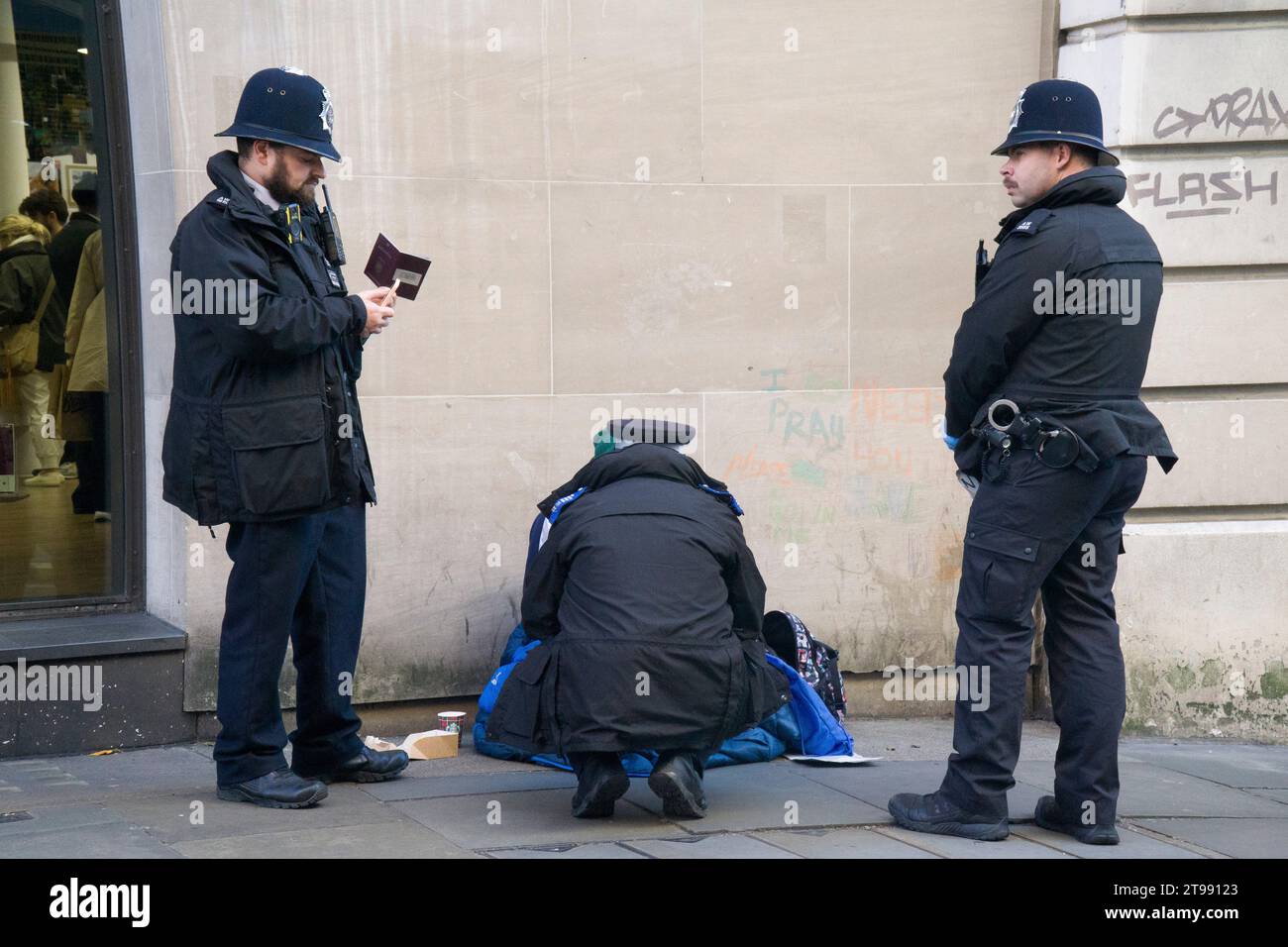 London, UK. 23rd Nov, 2023. Three police officers check the passport of a person who was begging on Long Acre, Covent Garden, having torn up the sign he was holding which said they were hungry. Credit: Anna Watson/Alamy Live News Stock Photo