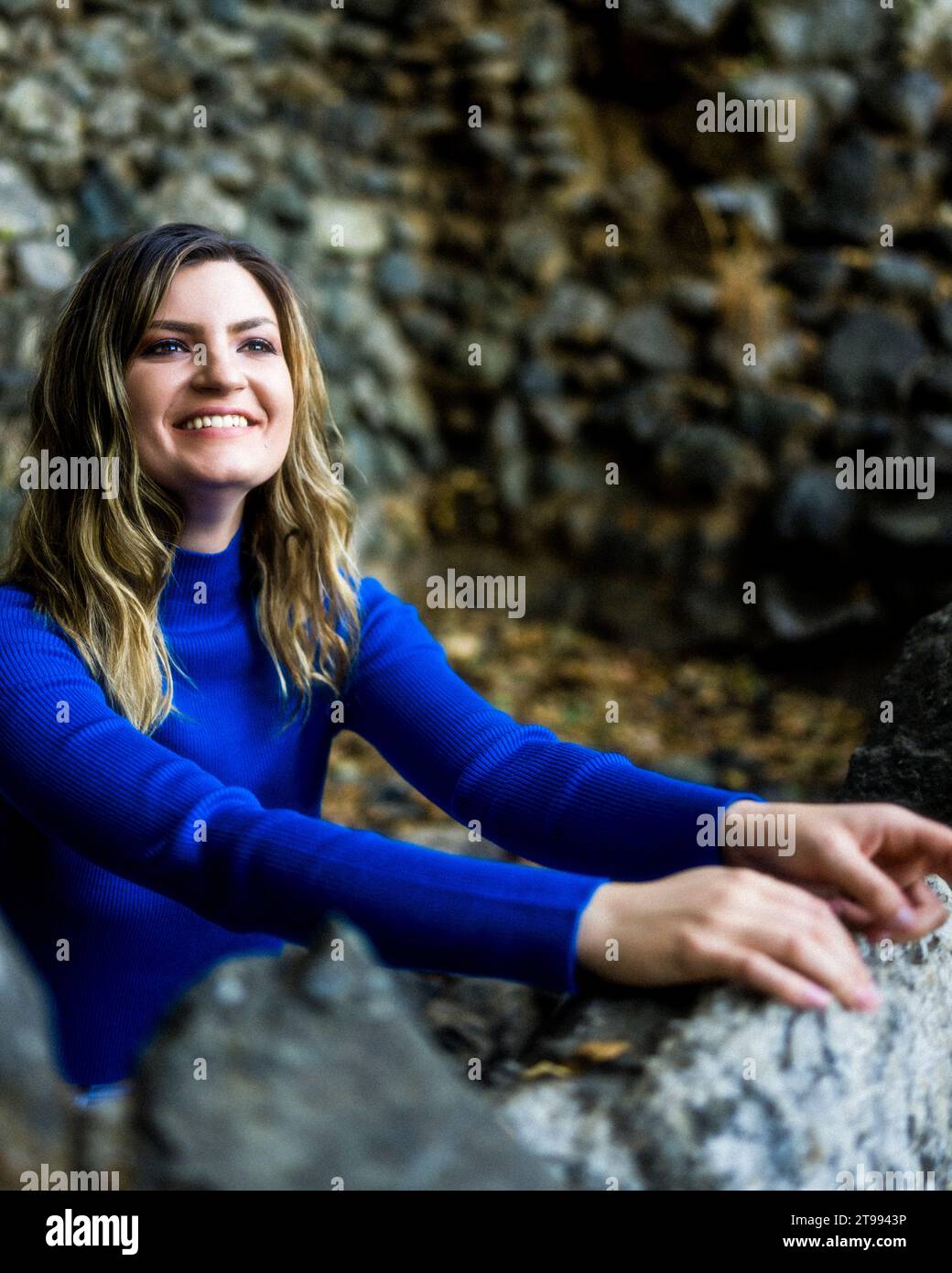 Young Woman Wearing Blue Long Sleeve Crop Top and White Denim Jeans Standing in a Old Rock Walled Fountain Stock Photo