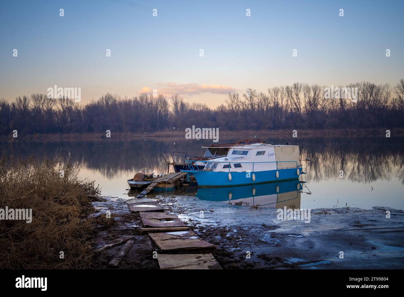 A white and blue boat docked in a tranquil river, surrounded by lush ...