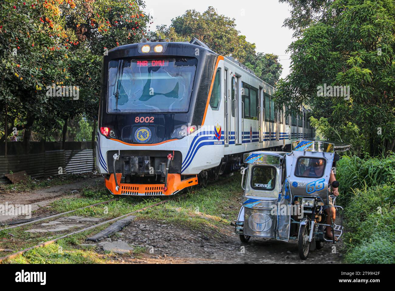 Manila, Philippines. November 24, 2023 : A tricycle drives near a diesel multiple unit PNR 8000 class train (manufactured in Indonesia) operated as Interprovincial Commuter by the Philippine National Railways (PNR) that celebrate today its 131th anniversary. The Philippines is implementing an ambitious rail expansion that involves stopping operations for 5 years in the National Capital Region (Metro Manila) from January 2024, which will affect about 30,000 Filipinos daily, to give way for the construction of the North-South Commuter Railway (NSCR) project. Credit: Kevin Izorce/Alamy Live News Stock Photo