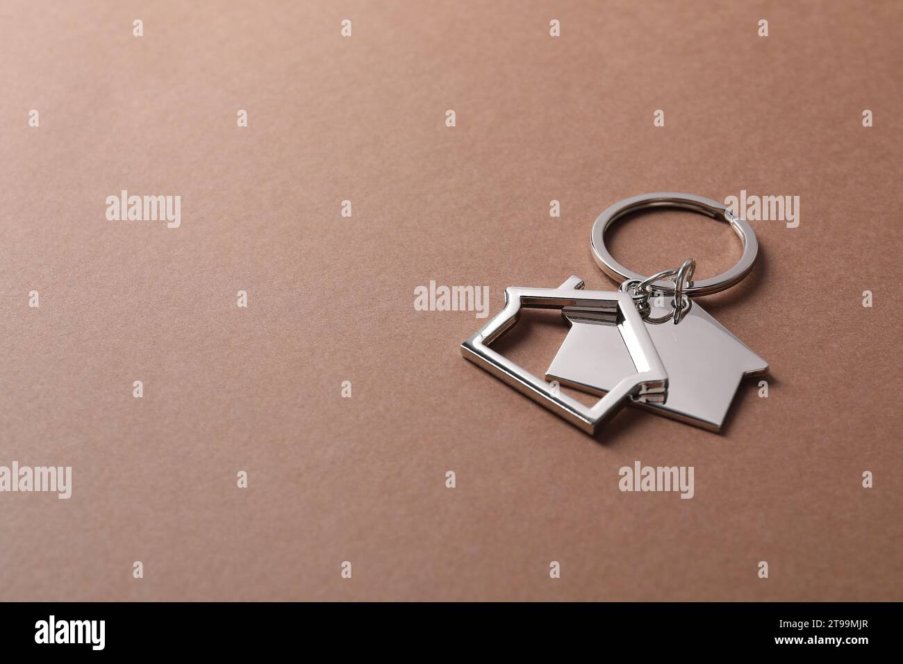 Metallic keychains in shape of houses on light brown background. Space ...