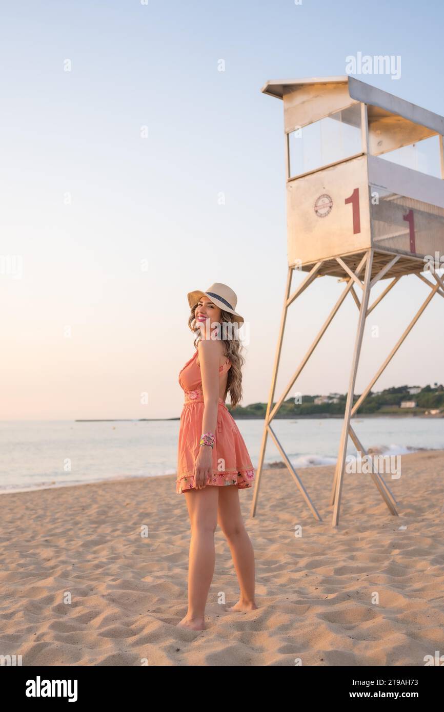 Vertical photo with copy space of a woman in summer clothes standing on a sandy beach during sunset Stock Photo