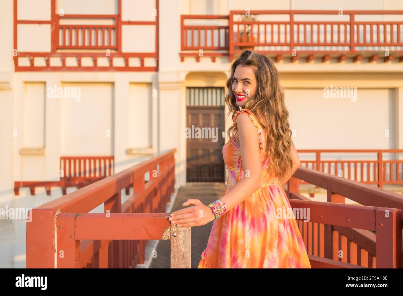 Pretty woman with long dress turning to smile at camera during sunset in a coastal bridge Stock Photo