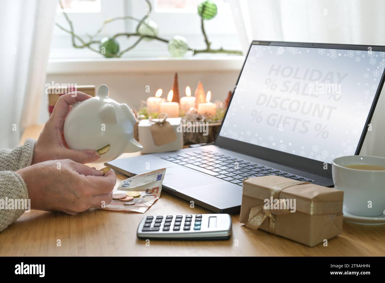 Womans hands shaking coins out of a piggy bank while shopping online for Christmas presents to take advantage of holiday discount offers on a table wi Stock Photo