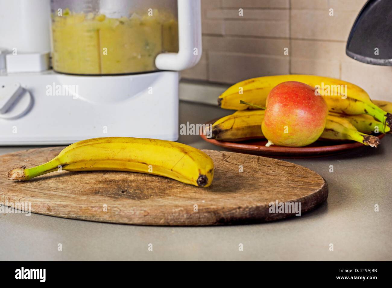 mashing bananas and apples and plums in a food processor in the kitchen