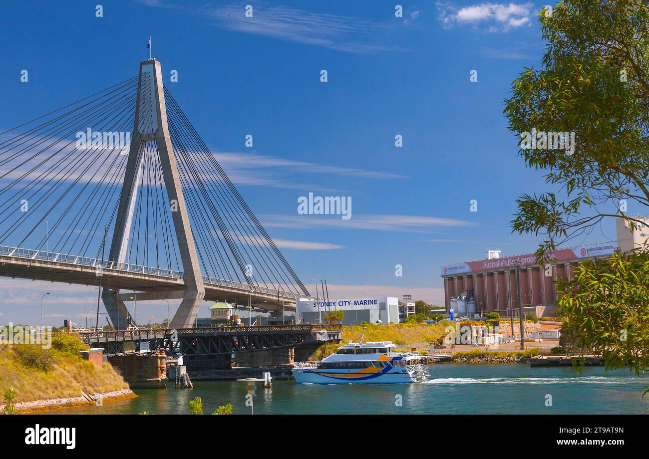 A sailboat travels beneath a bridge with an urban skyline in the distance Stock Photo