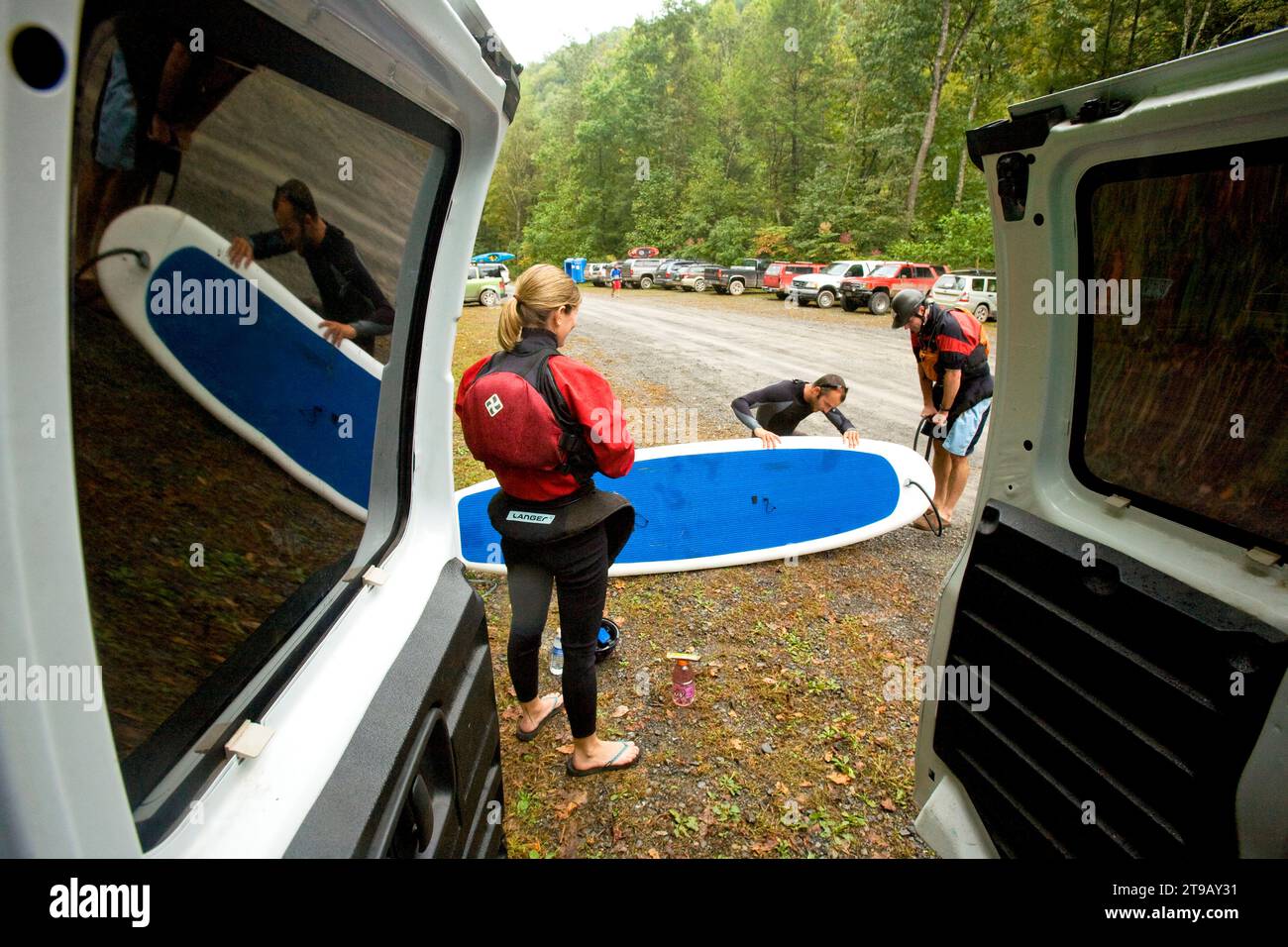 Woman watches while two men inflate a stand up paddleboard. Stock Photo