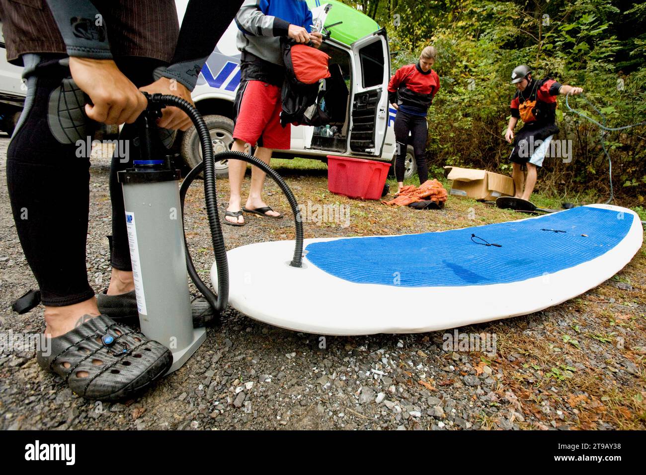 Man inflating a stand up paddleboard with friends getting ready to go kayaking. Stock Photo
