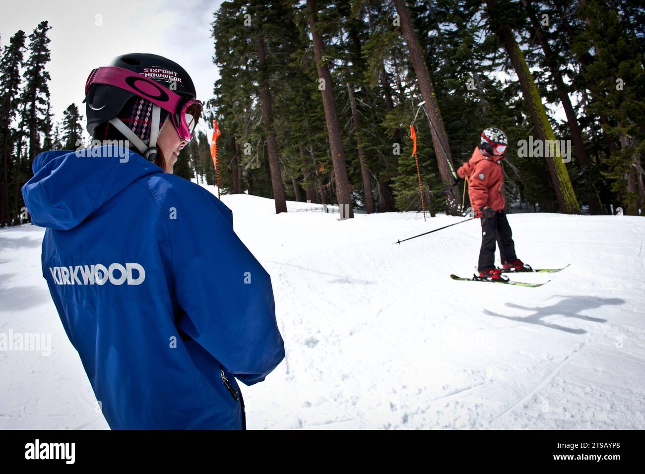Young skier jumping in a terrain park while his instructor looks on. Stock Photo