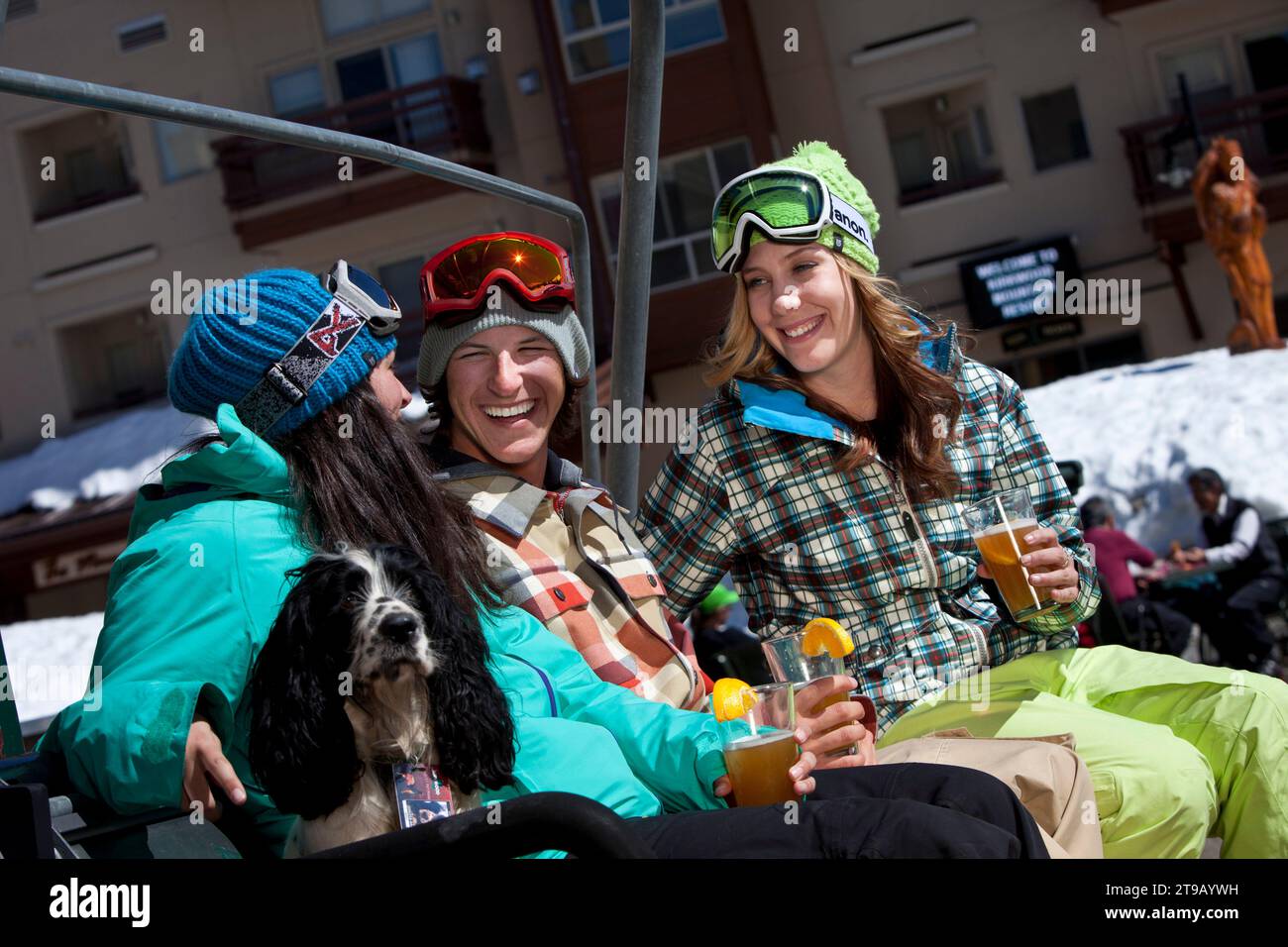 Three friends (one male and two females) hanging out with beers and a dog in front of a ski resort. Stock Photo
