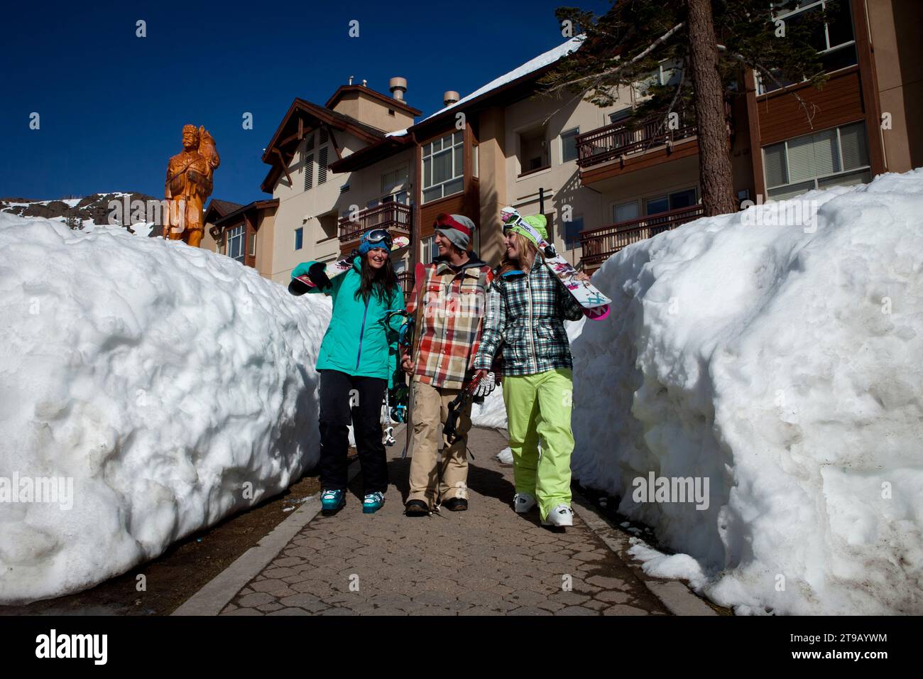 Three friends walking through the village at a ski resort with their skis. Stock Photo