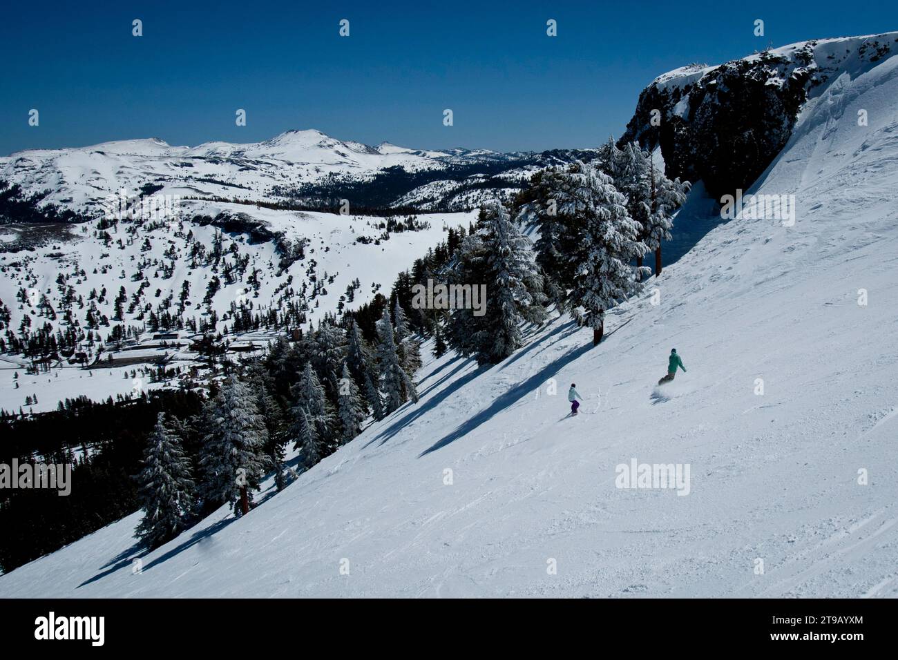 Two snowboarders riding spring conditions with a nice view. Stock Photo