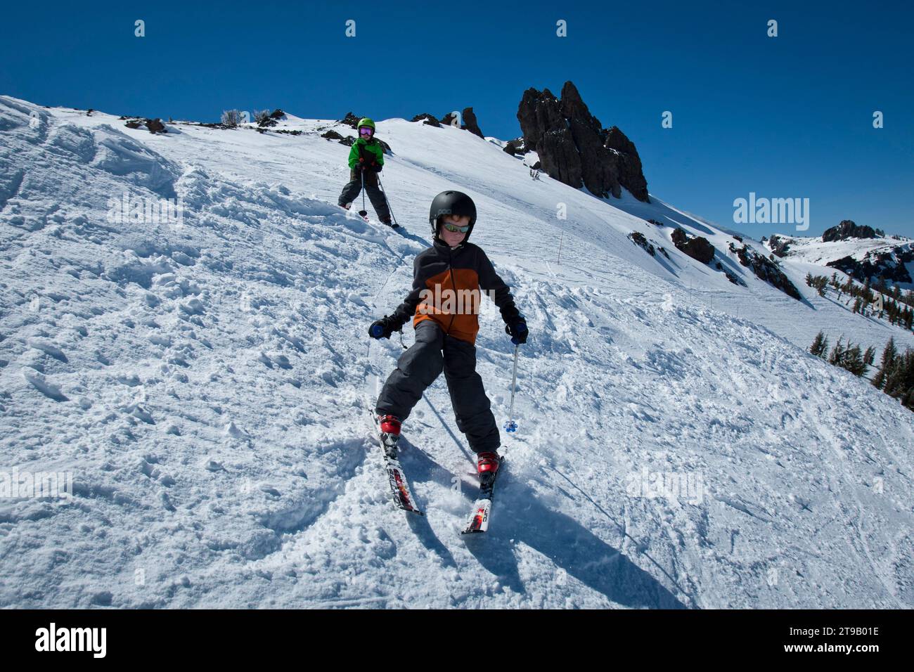 Two young skiers skiing down steep terrain. Stock Photo