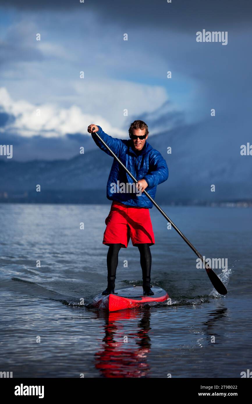 One man standup paddleboarding on a mountain lake in winter with a storm approaching. Stock Photo