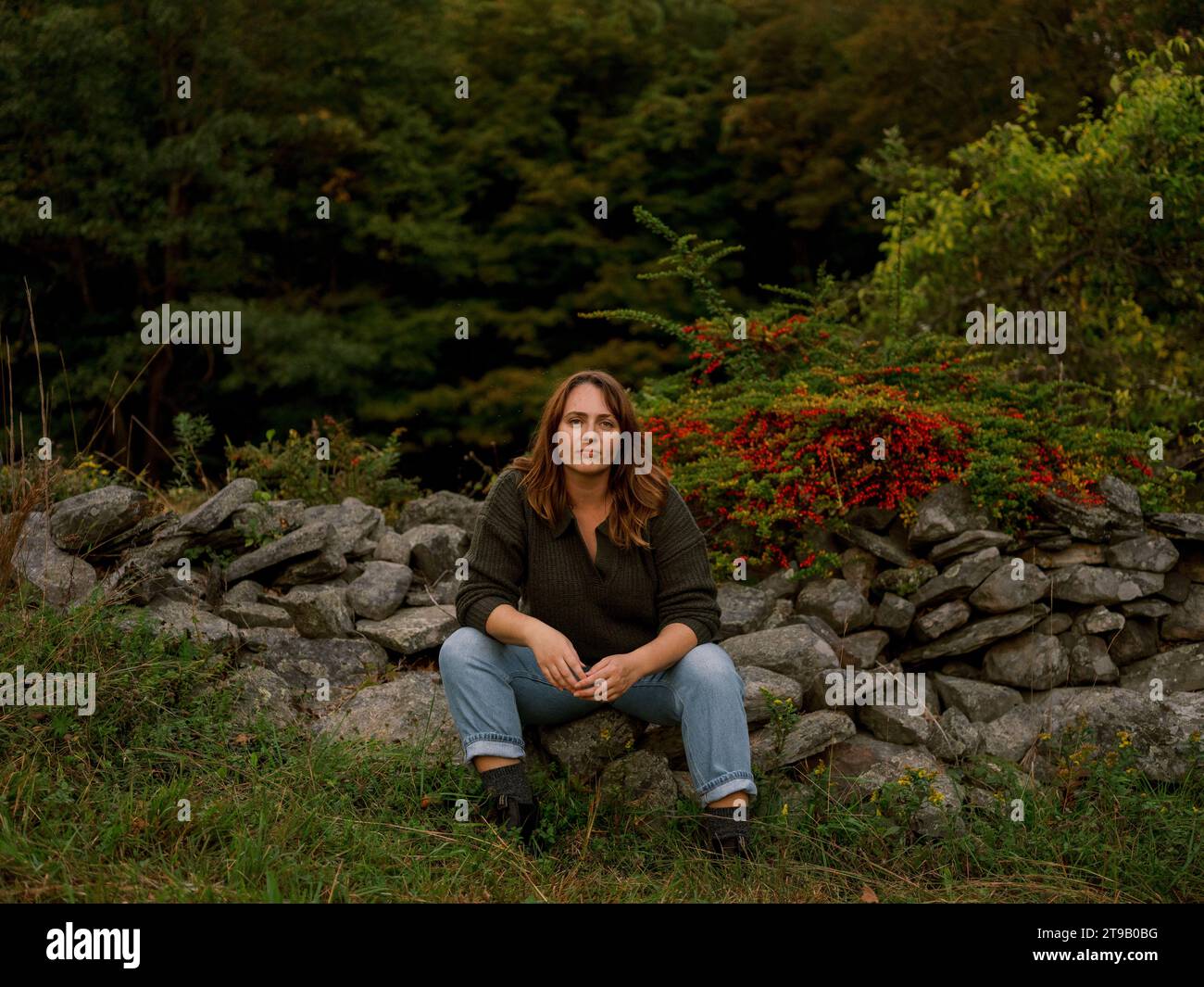Woman sitting in forest, serious expression, facing camera among Stock Photo