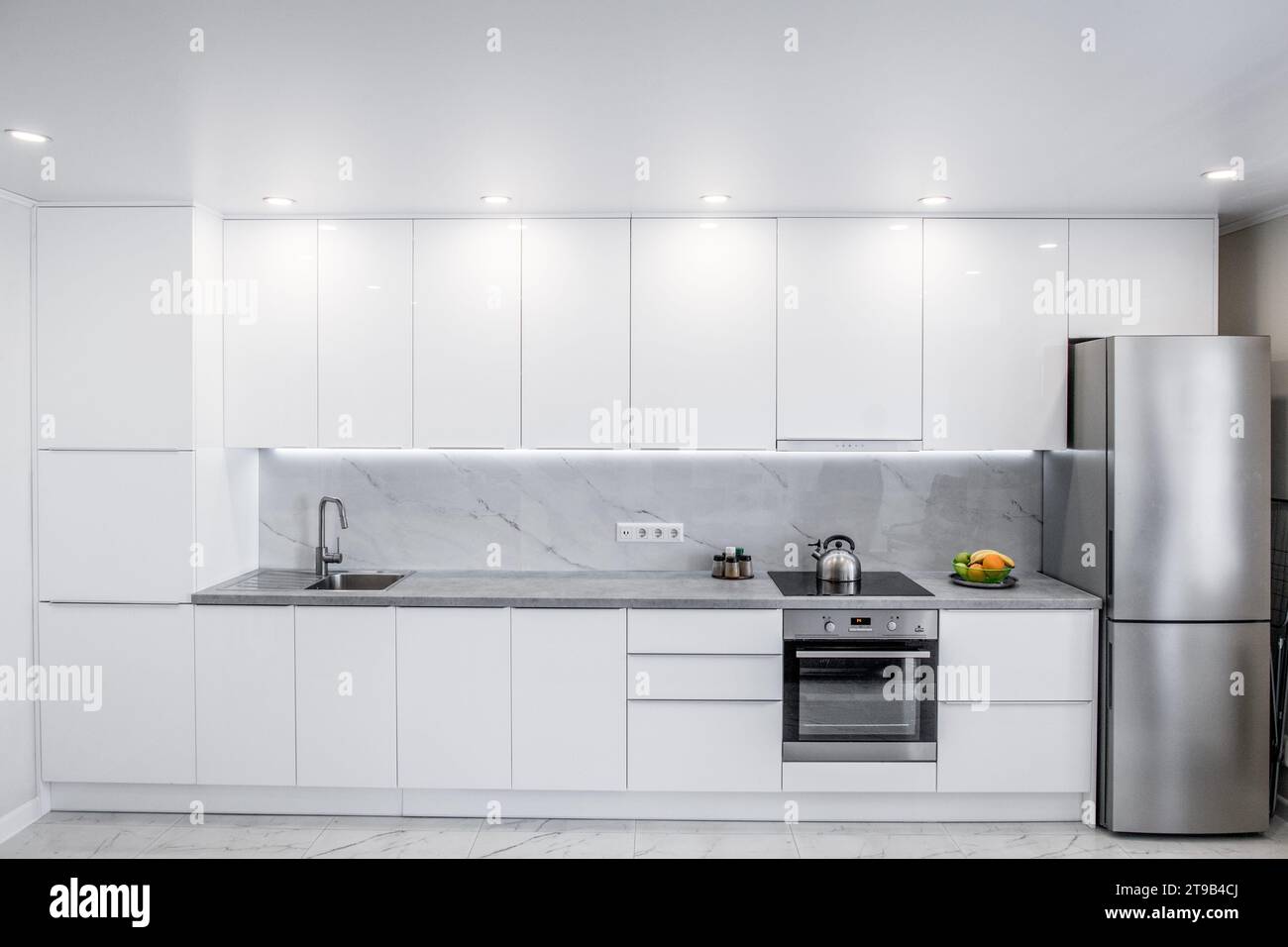 Front view of a modern white kitchen with many cabinets and all the necessary built-in appliances Stock Photo
