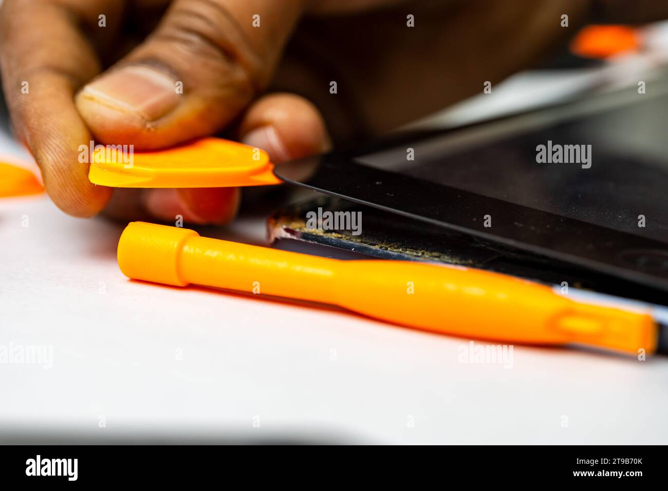 A skilled technician meticulously removes a tablet's display using specialized tools Stock Photo