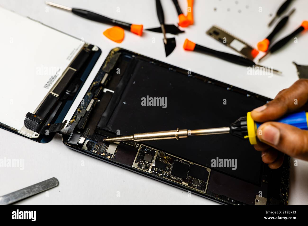 technician meticulously solders a tablet component using specialized tools in a well-lit workspace Stock Photo