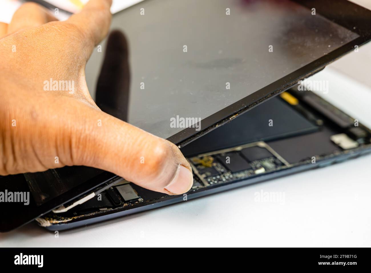 A skilled technician meticulously separates the cracked display from a tablet device using specialized tools Stock Photo