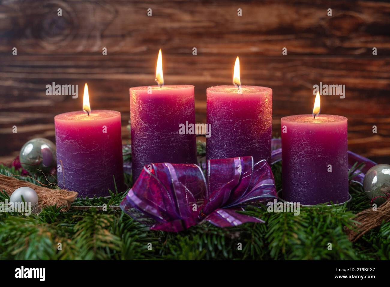 Augsburg, Bavaria, Germany - November 24, 2023: Christmas wreath with four burning purple candles for Advent *** Weihnachtskranz mit vier brennenden lila Kerzen zur Adventszeit Stock Photo