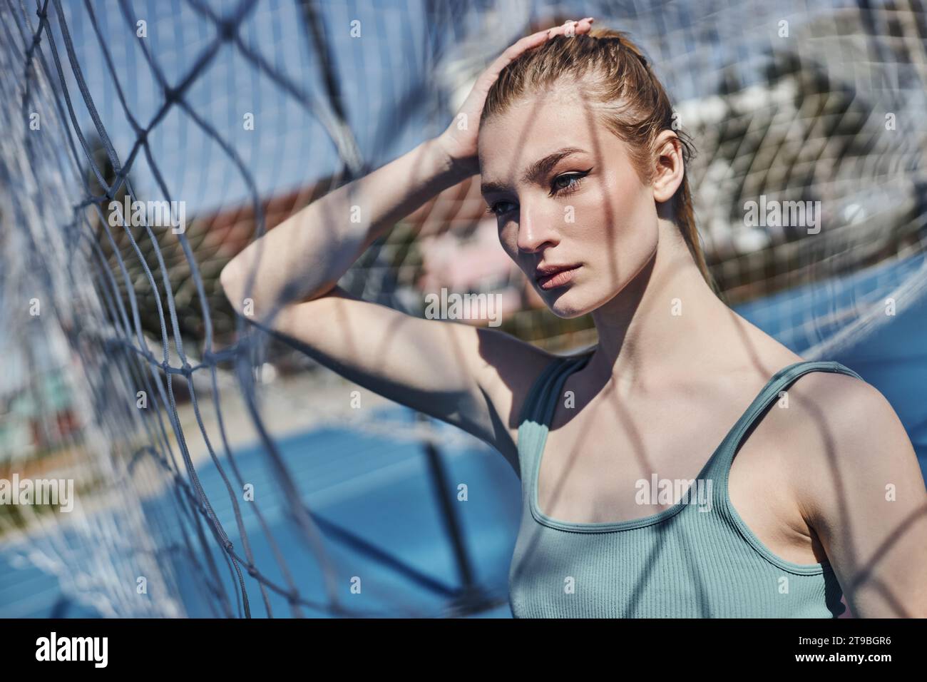 portrait of blonde and fit woman standing in activewear near net after working out outdoors Stock Photo