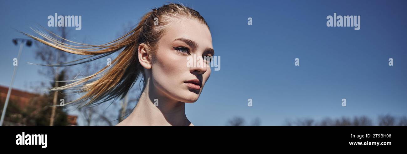 portrait of blonde young sportswoman with ponytail looking away after working out outdoors, banner Stock Photo